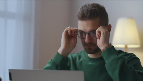 young-man-is-working-with-laptop-at-home-and-putting-on-glasses-for-good-vision-and-protection-eyes-portrait-of-guy-in-room